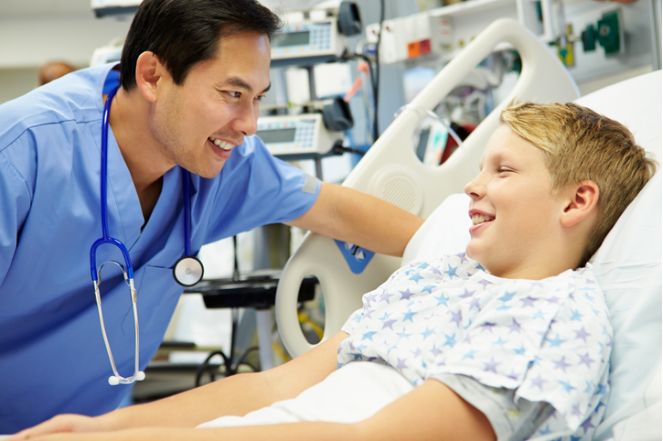 male nurse holding phone in blue scrubs with stethescope around neck smiles at camera