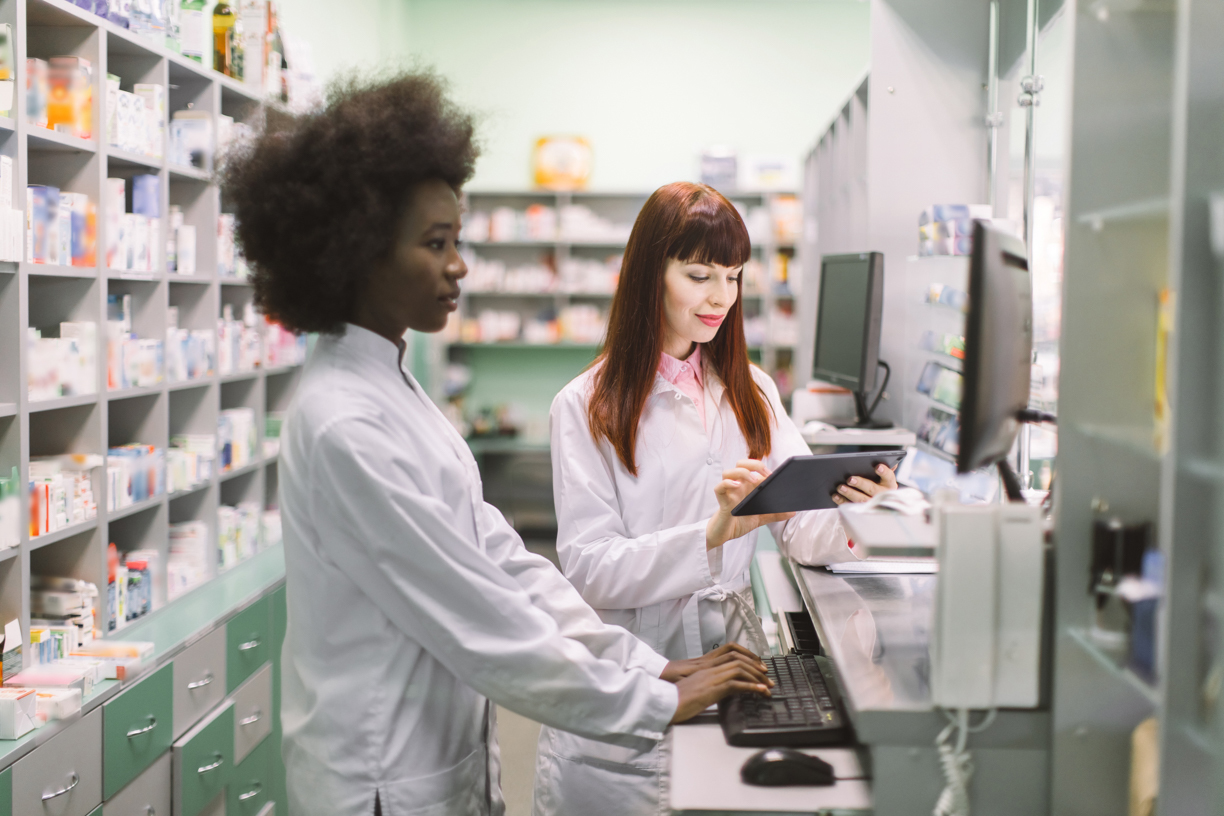 two pharmacy technicians look something up together on computers in store
