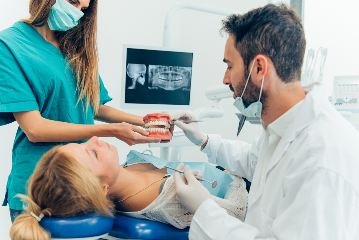 Dental assistant helps dentist show patient mouth model