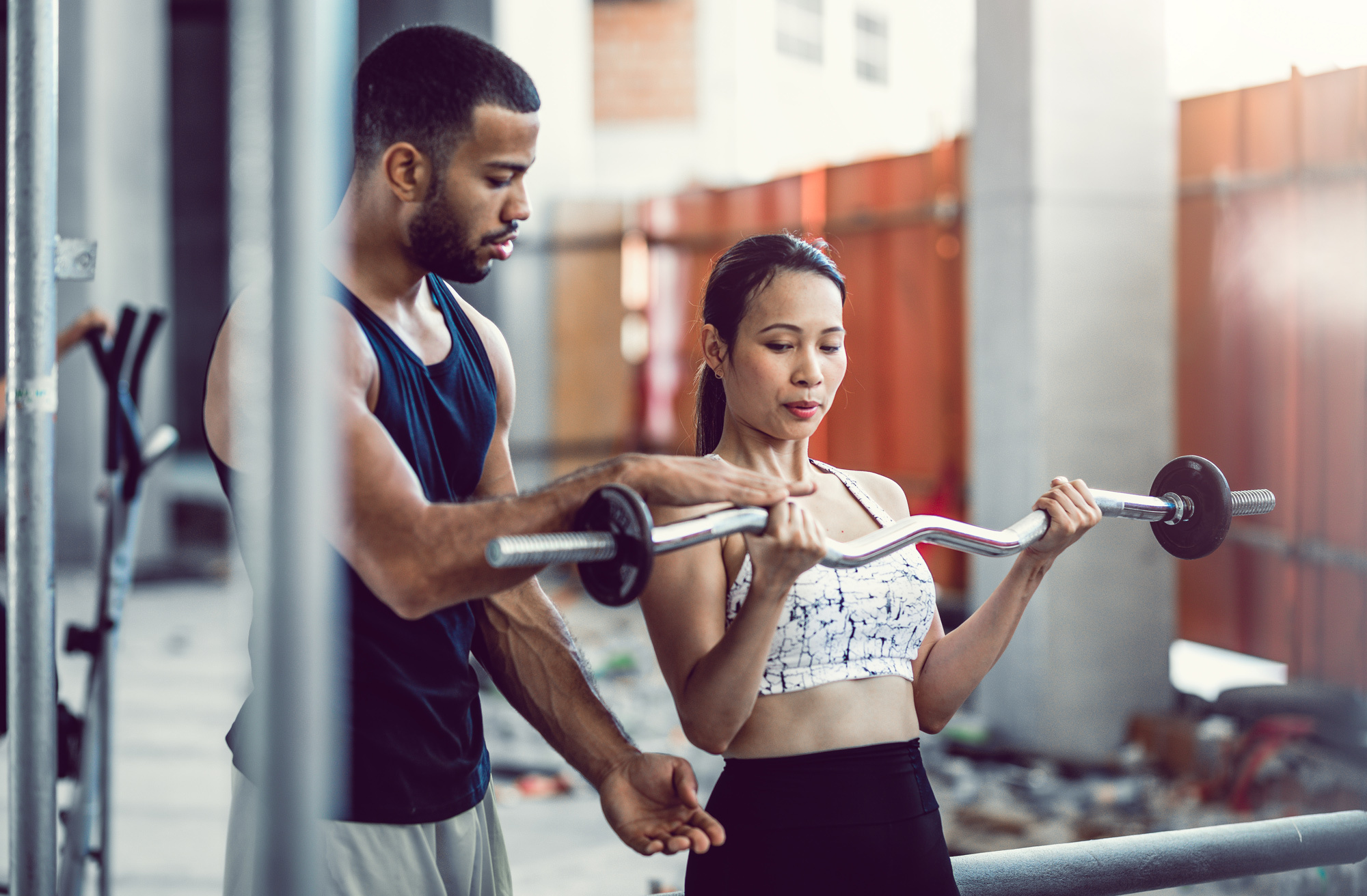 personal trainer guides woman lifting barbell